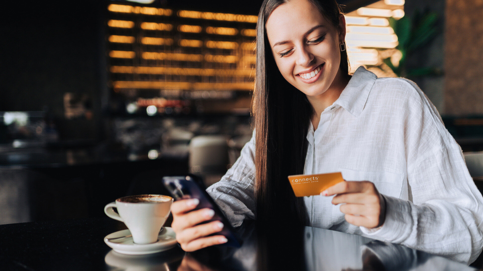 connects-li-cover-photo-1 A photo of a woman in a restaurant holding her phone and a credit card from Connects FCU, a credit union in Richmond Virginia.