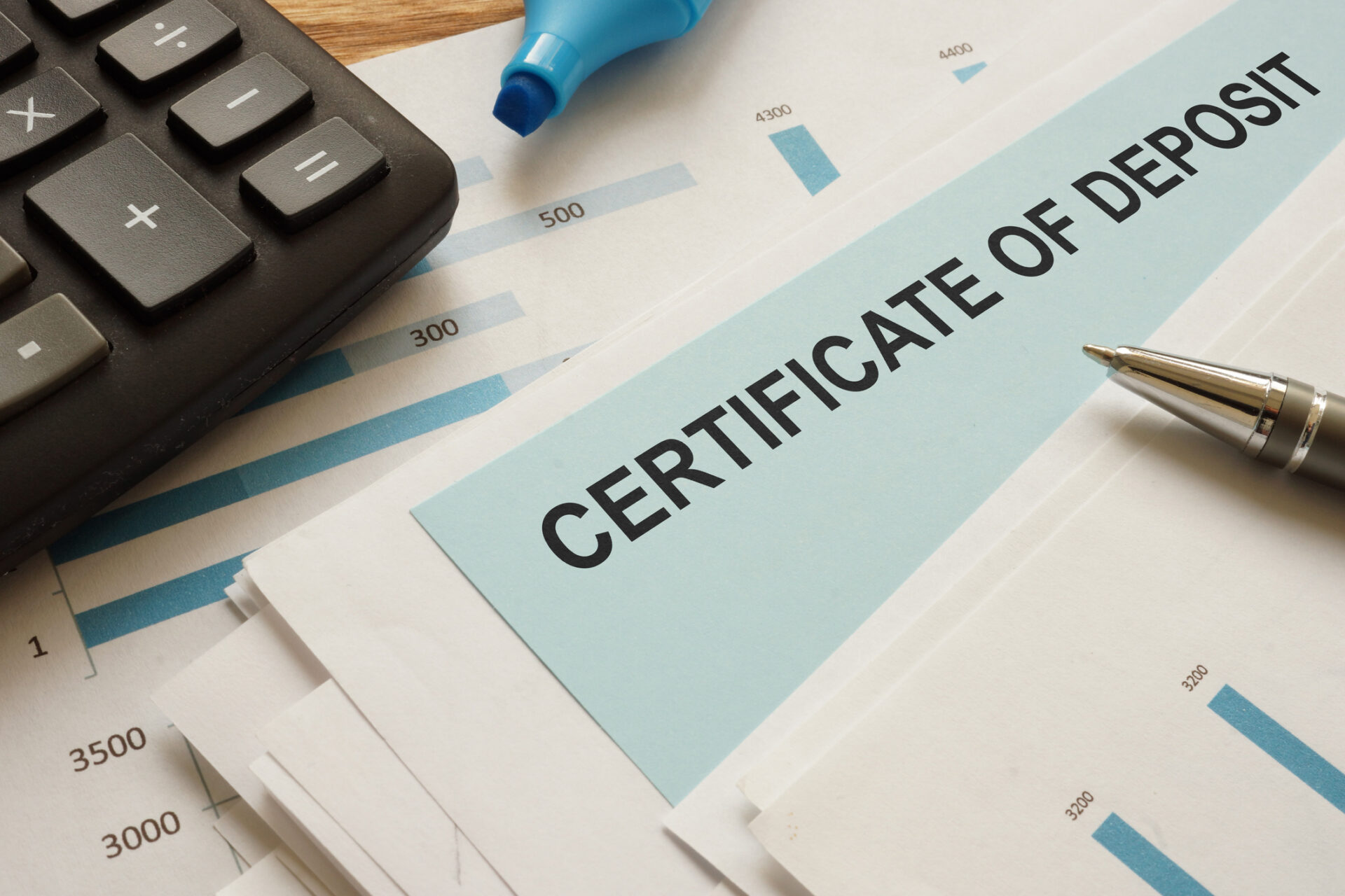 Certificate of deposit document on a desk with a pen, calculator, and financial graphs in the background, conveying banking planning.